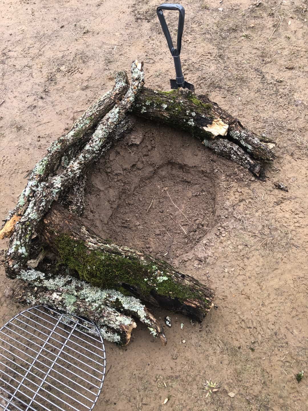 a hand dug campfire pit with a log heat reflector and wind break.