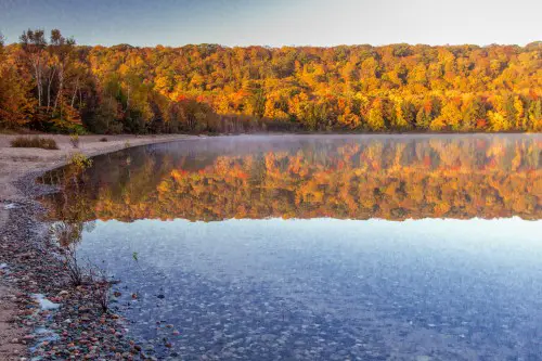 This is a photograph of Hiawatha National Forest in autum as the leaves change to beautiful orange and red colors overlooking a blue lake.