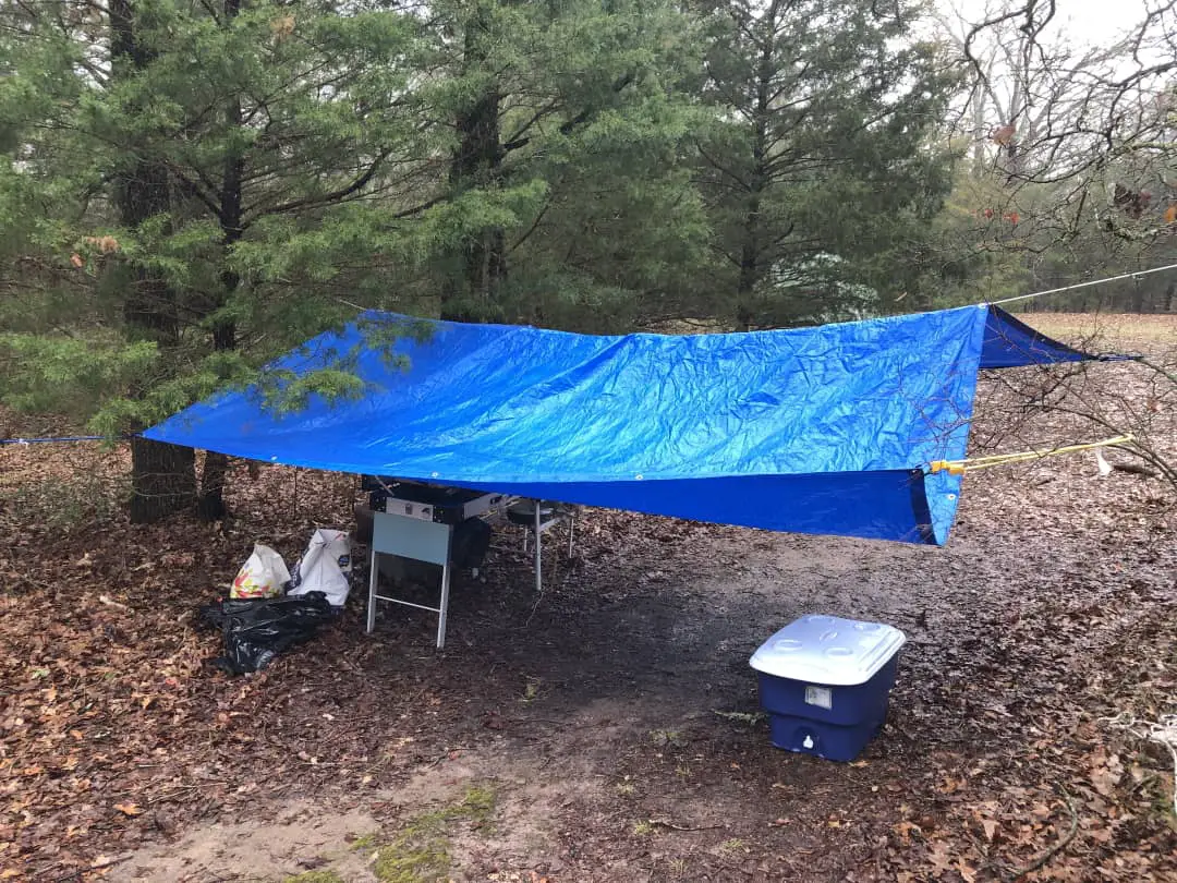 A tarp tied to a set of trees to keep a camp kitchen area dry in a rain storm.